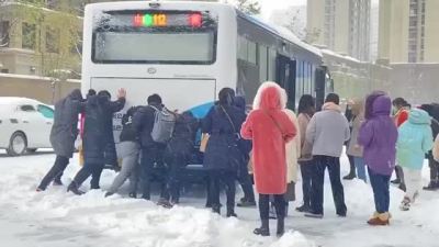 公交车陷雪中无法前行 多名乘客主动下来推车